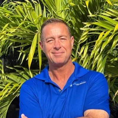 Chiropractor Gregory Dokka Smiling In Front Of Greenery